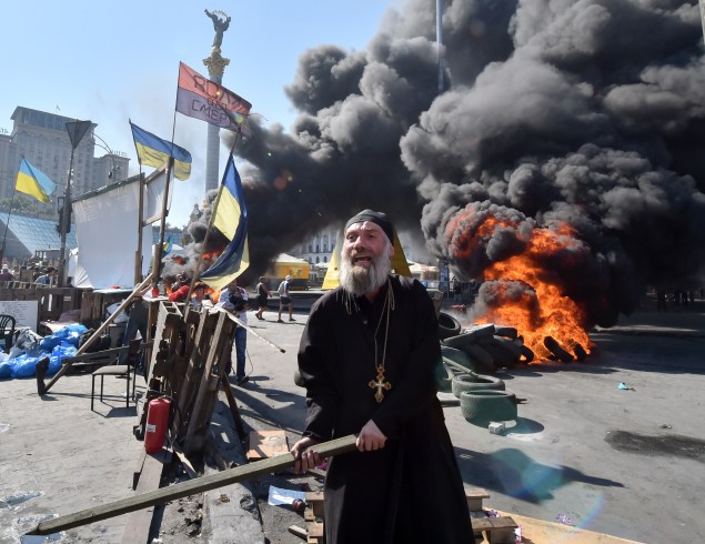 An Orthodox priest gestures with a stick as Maidan self-defence activists clash Kiev-1 volunteer battalion in Kiev. (Photo by Sergei Supinsky/AFP/Getty Images)