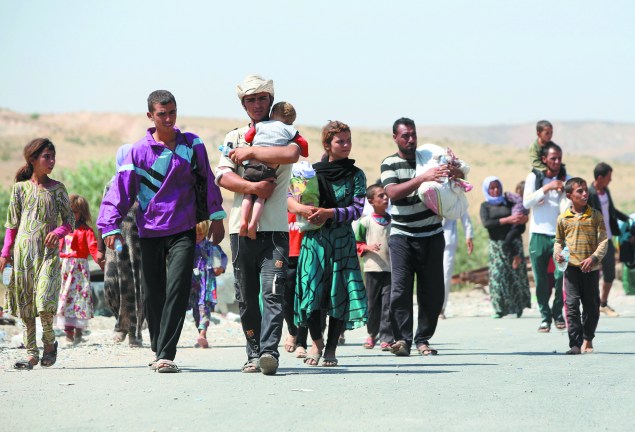 Displaced Iraqis from the Yazidi community carry their children as they cross the Iraqi-Syrian border.