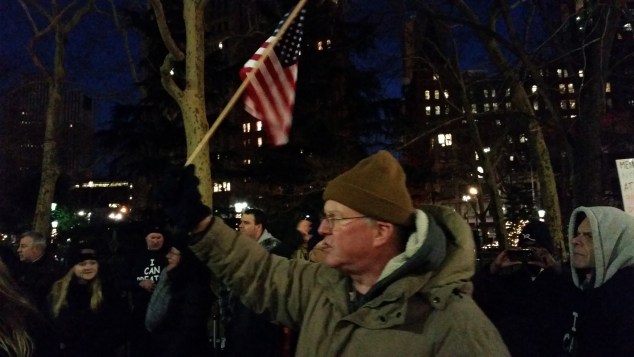 A supporter of the NYPD raises an American flag at a rally tonight. (Photo: Ross Barkan)