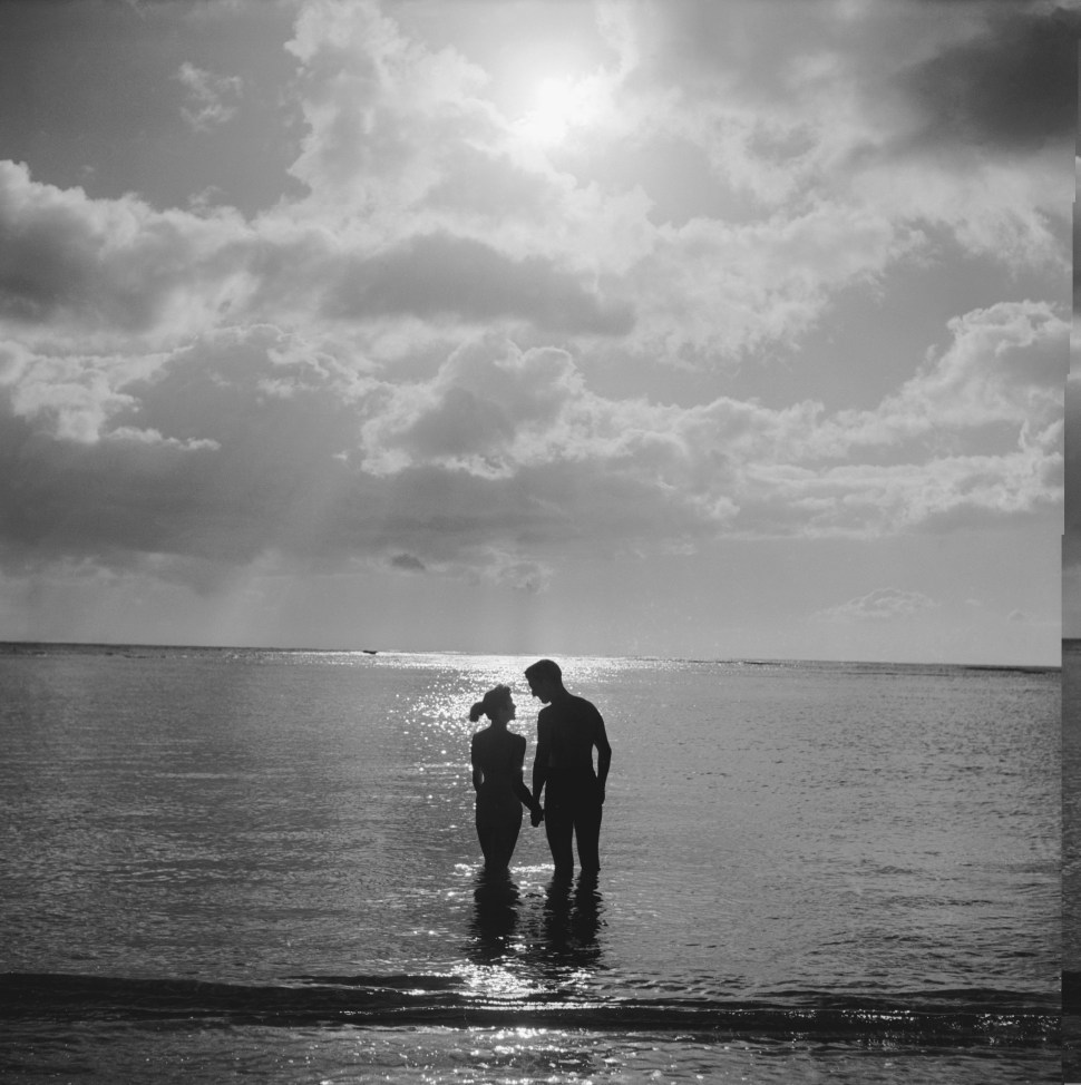 Circa 1955: a young couple on their honeymoon in Hawaii enjoy the romance of a sunset dip in the Pacific Ocean. (Photo: Orlando /Three Lions/Getty Images).