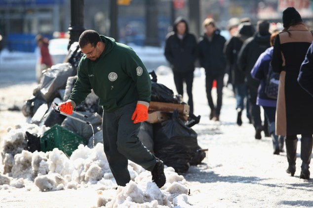 A sanitation worker moves garbage ahead of a snow plow at Union Square. (Photo: John Moore/Getty Images)