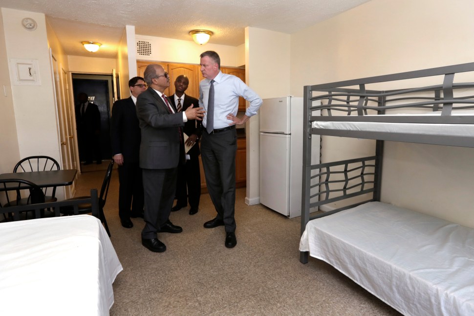 NEW YORK, NY - MAY 11: New York Mayor Bill de Blasio, right, listens to Acacia Network CEO Raul Russ, foreground left, as he visits a room at the Corona Family Residence, a homeless facility, May 11, 2015 in the Queens borough of New York City. Mayor deBlasio made an announcement on his effort to combat the city's homelessness crisis. Also in the visit are Dept. of Investigations Commissioner Mark Peters, background left, and Dept. of Homeless Services Commissioner Gilbert Taylor.