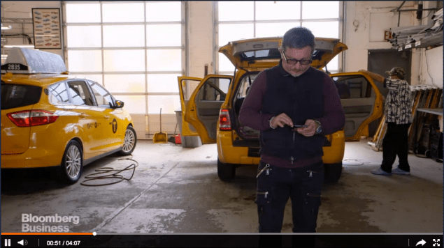 Borderline millennial Gene Freidman taps some sort of technological device in one of the many garages housing taxis he owns. (Bloomberg Business screencap)