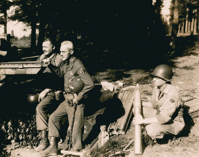 Hemingway, at left, beside Col. Charles ‘Buck’ Lanham in Germany during World War II. An unidentified soldier kneels to hold ammunition. (