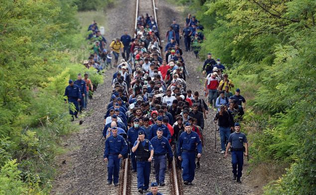 Refugees of different countries accompanied by police officers walk on the railway tracks near Szeged town as they broke out from the migrant collection point near Roszke village of the Hungarian-Serbian border on September 8, 2015. Hungary's border with Serbia has become a major crossing point into the European Union, with more than 160,000 entering Hungary so far this year including 2,706 on September 7, 2015 alone, police said. AFP PHOTO / ATTILA KISBENEDEK (Photo credit should read ATTILA KISBENEDEK/AFP/Getty Images)