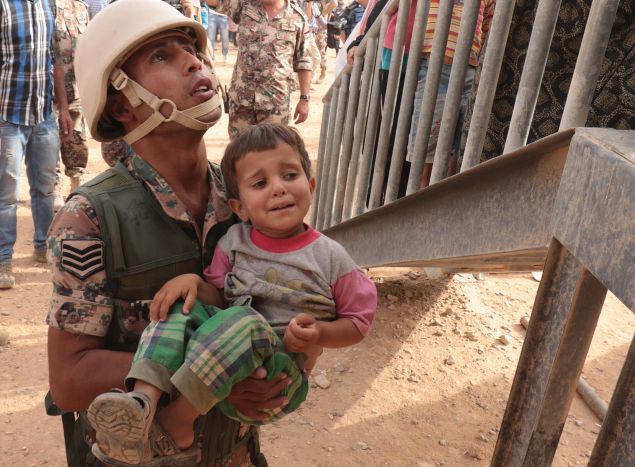 A Jordanian soldier carries a young Syrian refugee at the al-Roqban makeshift camp, on the border with Syria, before driving a group of refugees to the eastern town of Ruwaished where they will be welcomed and checked by the Jordanian authorities on September 10, 2015. The latest batch of refugees from neighbouring Syria will be sent from Ruwaished, around 380 km from the capital Amman, to various refugee camps and temporary settlements across the country. AFP PHOTO / KHALIL MAZRAAWI (Photo credit should read KHALIL MAZRAAWI/AFP/Getty Images)