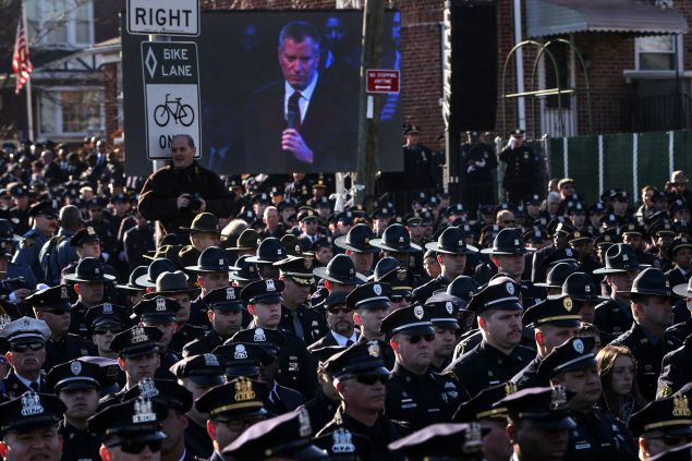 Law enforcement officers turn their backs on a live video monitor showing New York City Mayor Bill de Blasio as he speaks at the funeral of slain New York Police Department (NYPD) officer Rafael Ramos near Christ Tabernacle Church in the Queens borough of New York December 27, 2014. Tens of thousands of police and other mourners filled a New York City church and surrounding streets for the funeral on Saturday of one of two police officers ambushed by a gunman who said he was avenging the killing of unarmed black men by police. Singled out for their uniforms, the deaths of Rafael Ramos and his partner Wenjian Liu have become a rallying point for police and their supporters around the country, beleaguered by months of street rallies by protesters who say police practices are marked by racism. REUTERS/Shannon Stapleton (UNITED STATES - Tags: CIVIL UNREST POLITICS CRIME LAW TPX IMAGES OF THE DAY) - RTR4JDQZ