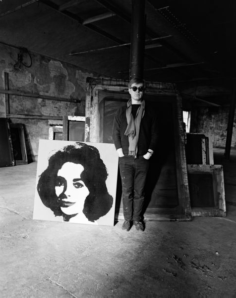 Evelyn Hofer, Andy Warhol standing in the Factory with a Liz painting and several screens in the background, January 29, 1964. (Photo: The Estate of Evelyn Hofer)