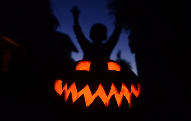 Children play behind a pumpkin carved and lit for Halloween, on October 30, 2013 in Monterey Park, California, a day before the annual celebration of the traditional All Hallow's Eve, the time in the liturgical year dedicated to remembering the dead, including saints (hallows), martyrs, and faithful departed believers. AFP PHOTO/Frederic J. BROWN (Photo credit should read FREDERIC J. BROWN/AFP/Getty Images)