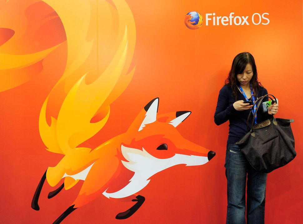 A woman looks at her mobile phone as she stands in front of a poster of Mozilla Firefox on February 27, 2013 at the Mobile World Congress, the world's biggest mobile fair, in Barcelona. The European Union warned member states on February 26 to free up the airwaves for new, super-fast fourth generation mobile networks and threatened legal action against those that deliberately block the process. AFP PHOTO/JOSEP LAGO