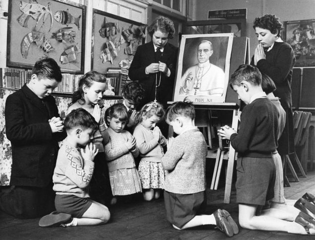 Pupils from the Italian Roman Catholic School in Clerkenwell, London, kneel before a picture of Pope Pius XII as his life hangs in the balance following a second stroke. (Photo by Reg Speller/Getty Images)