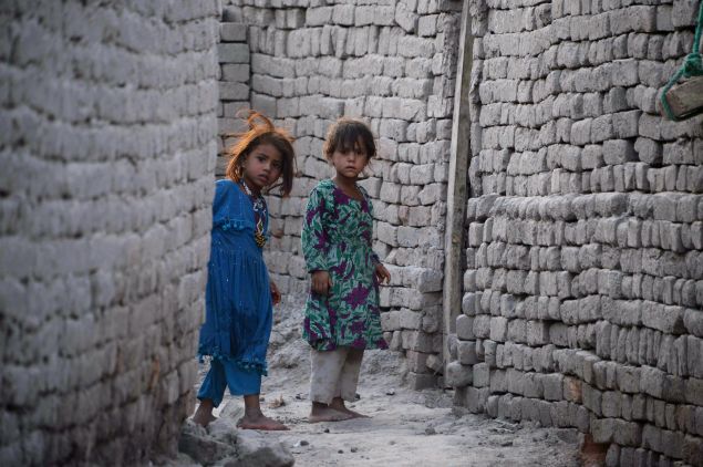 In this photograph taken on July 5, 2015, Afghan girls who fled from Kot district of the eastern Nangarhar' province, following threats from the Islamic State group to leave their homes, look around a corner next to their temporary homes in Jalalabad. Authorities said more than 250 families had moved from Kot district of the eastern province to Jalalabad, with representatives of the displaced families telling AFP that Islamic State fighters had ordered families whose members were working for the government or Afghan National Security Forces to leave their homes. AFP PHOTO / Noorullah Shirzada (Photo credit should read Noorullah Shirzada/AFP/Getty Images)