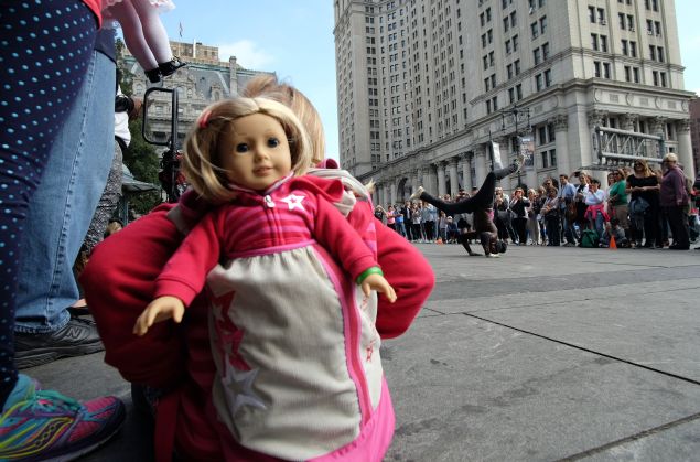 A girl with her doll peeking out of her backpack watches as a street entertainer dances during a road side show in New York on October 9, 2015. AFP PHOTO/JEWEL SAMAD (Photo credit should read JEWEL SAMAD/AFP/Getty Images)
