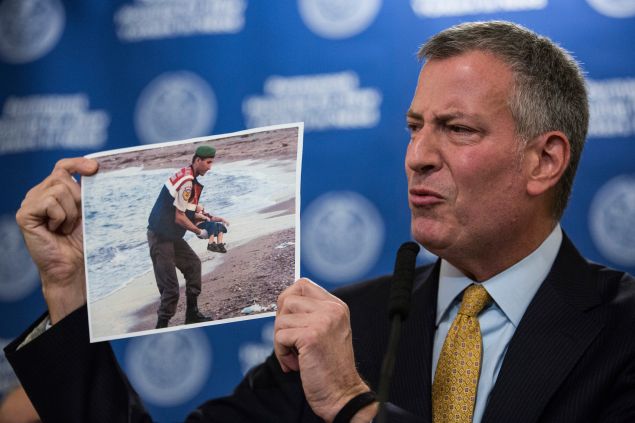 New York City Mayor Bill de Blasio holds up a photo of a the body of a dead child refugee being recovered from a beach (Photo: Andrew Burton for Getty Images)
