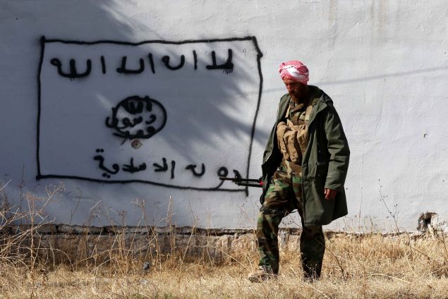 A Kurdish fighter walks by a wall bearing a drawing of the flag of the Islamic State (IS) group in the northern Iraqi town of Sinjar, in the Nineveh Province, on November 13, 2015. Iraqi Kurdish leader Massud Barzani announced the "liberation" of Sinjar from the Islamic State group in an assault backed by US-led strikes that cut a key jihadist supply line with Syria. AFP PHOTO / SAFIN HAMED / AFP / SAFIN HAMED (Photo credit should read SAFIN HAMED/AFP/Getty Images)
