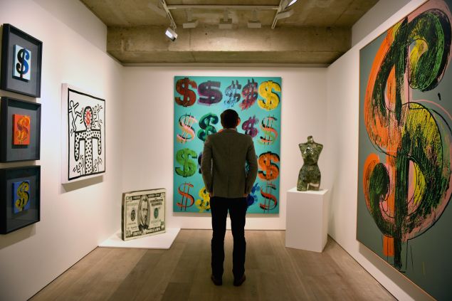 LONDON, ENGLAND - JUNE 08: A visitor studies 'Dollar Signs', 1981, by Andy Warhol which has an estimated value of £4.5-6.5 million and is going on show at Sotheby's on June 8, 2015 in London, England. The work is a centrepiece of an exhibition of 21 pieces inspired by the US Dollar which are estimated to have a total value of £50 million and will go under offer by the auction house on 1st and 2nd July 2015. (Photo by Mary Turner/Getty Images)