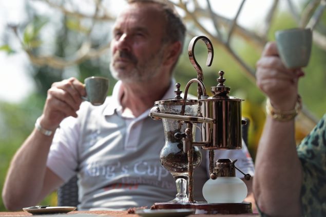 TO GO WITH Thailand-lifestyle-elephant-coffee, FEATURE by Marion THIBAUT This picture taken on April 10, 2015 shows German tourist Gerd Schautz drinking a cup of Black Ivory Coffee at the luxury Anantara resort, home to the Golden Triangle Asian Elephant Foundation, in the Thai northern town of Chiang Saen, near the border with Myanmar and Laos. In the verdant hills of northern Thailand, a mahout collects a large pile of elephant dung, studded with coffee beans. Ingested by pachyderms the day before, these excreted beans will produce one of the world's most expensive coffees. AFP PHOTO / Christophe ARCHAMBAULT