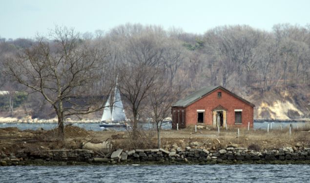 A sailboat passes behind an abandoned building on Hart Island on April 5, 2014 in New York. Each white plastic pipe near the building marks an infant mass gravesite, one plastic pipe per 1,000 babies. Hart Island, occupying 101 acres in the Long Island Sound on the eastern edge of the Bronx in New York, contains the largest cemetery in the US. One million bodies of still born babies, the poor, the unidentified and the unclaimed are buried by prison labor in common graves. It is run by the department of corrections, and access is nearly impossible. AFP PHOTO/Don Emmert (Photo credit should read DON EMMERT/AFP/Getty Images)