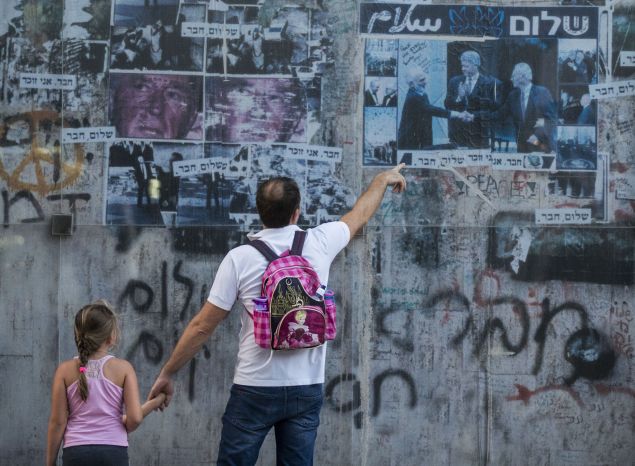 An Israeli father shows to his daughter a 20-year-old picture of late Israeli prime minister Yitzhak Rabin (R) shaking hands with late Jordanian King Hussein (L) while former US president Bill Clinton applauds, on October 24, 2015 at a memorial at the place where Rabin was assassinated in the Israeli Mediterranean city of Tel Aviv in 1995 at the hands of a Jewish extremist opposed to peace with the Palestinians. Rabin was shot after giving a speech to tens of thousands of peace demonstrators in Tel Aviv. His killer, Yigal Amir, was a rightwing extremist opposed to the Oslo peace accords with the Palestinians, for which Rabin won the 1994 Nobel peace prize. AFP PHOTO / JACK GUEZ (Photo credit should read JACK GUEZ/AFP/Getty Images)