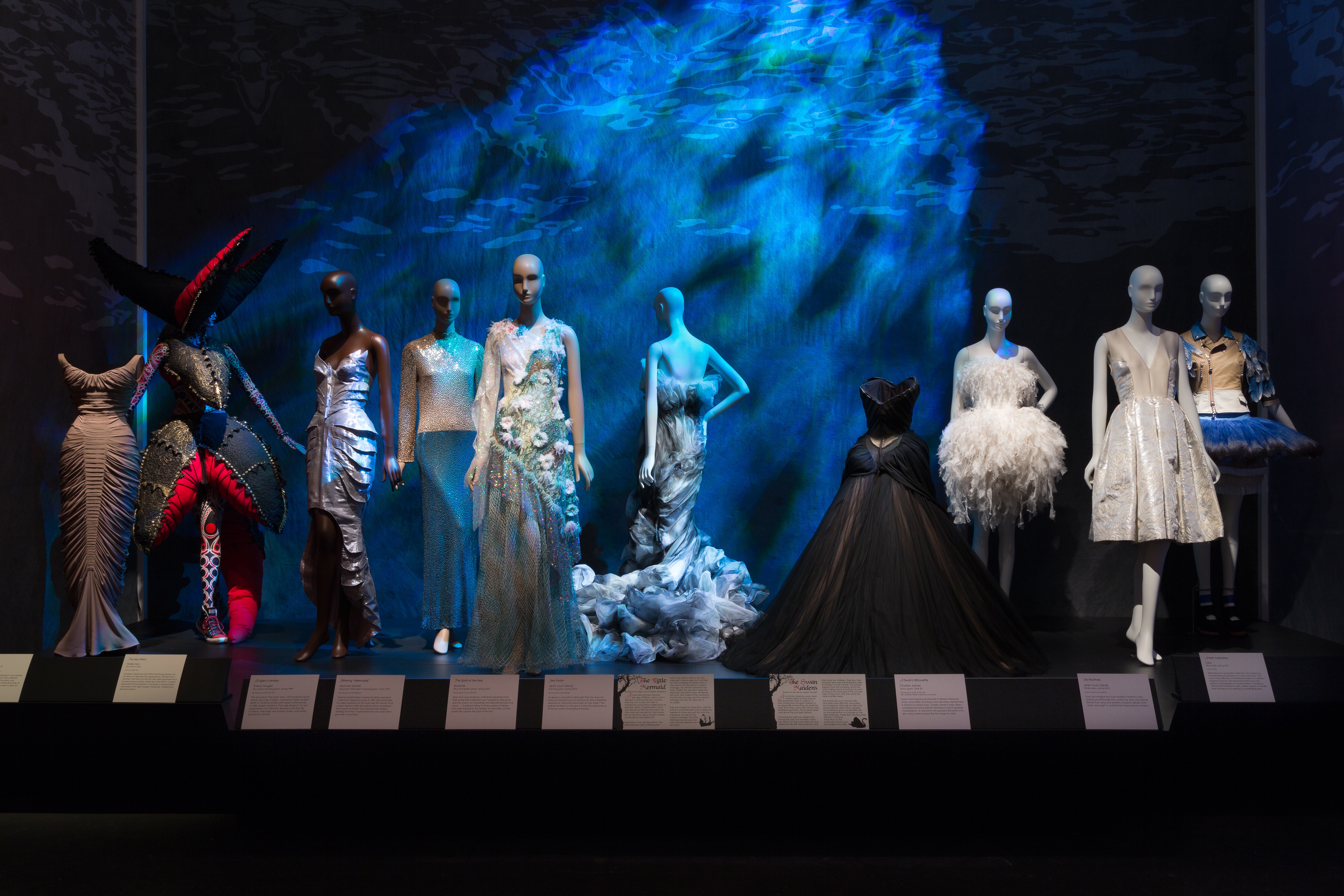 Clothing illustrating “The Little Mermaid” and “The Swan Maidens.” From left to right: clothing by Charles James, Hideki Seo, Thierry Mugler, Norman Norell, Rodarte, Jean Louis Sabaji, Charles James, Jean Louis Sabaji, Giles, and Undercover