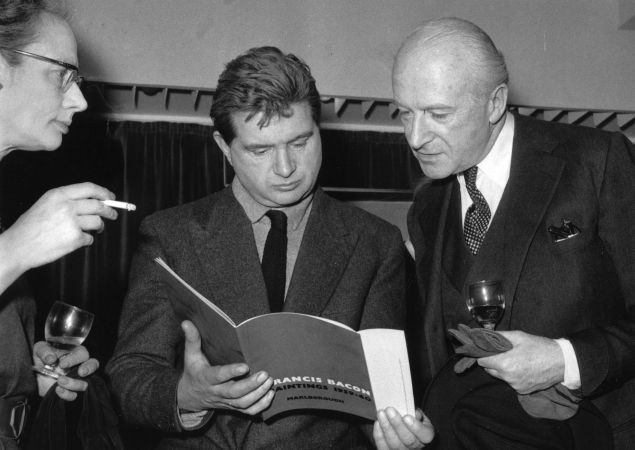Irish painter Francis Bacon (1909 - 1992) (centre), reading his exhibition catalogue, and English photographer Cecil Beaton at the Marlborough Gallery, London. (Photo by Evening Standard/Getty Images)