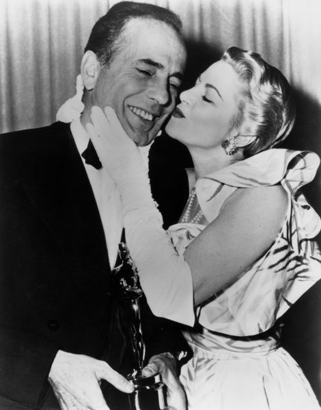 1952: American actor Humphrey Bogart (1899-1957) receives a kiss from actor Claire Trevor (1909 - 2000) while standing backstage with the Best Actor Oscar he won for his role in director John Huston's film, 'The African Queen,' RKO Pantages Theatre, Los Angeles, California.