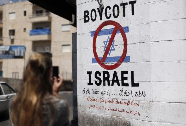 A tourist photographs a sign painted on a wall in the West Bank biblical town of Bethlehem on June 5, 2015, calling to boycott Israeli products coming from Jewish settlements. The international BDS (boycott, divestment and sanctions) campaign, that pushes for a ban on Israeli products, aims to exert political and economic pressure over Israel's occupation of the Palestinian territories in a bid to repeat the success of the campaign which ended apartheid in South Africa. AFP PHOTO / THOMAS COEX (Photo credit should read THOMAS COEX/AFP/Getty Images)