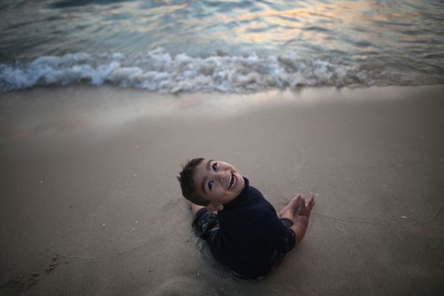 GAZA CITY, GAZA - JUNE 13: A young Palastinian boy laughs as the waves rush towards him on Gaza beach on June 13, 2015 in Gaza City, Gaza. Palestinians are taking the opportunity to relax and enjoy picnics on Gaza beach before the holy month of Ramadan which starts next week. Thousands of Palestinians descend on the 75km sandy beach of Gaza each day to relax, fish and escape the noise and heat of the city. The devastation across Gaza can still be seen nearly one year on from the 2014 conflict between Israel and Palestinian militants. Money pledged by the international community six months ago to rebuild Gaza has not materialised leaving many Palestinians impoverished and still suffering with the poor economy. (Photo by Christopher Furlong/Getty Images)