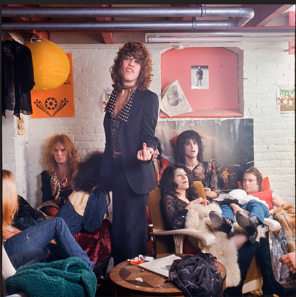 The New York Dolls in their dressing room at Paradiso, Amsterdam, Netherlands, 7th December 1973. L-R Arthur Kane (back left against wall), David Johansen (centre, raising middle finger), Johnny Thunders (part obscured behind Johansen), Sylvain Sylvain (leaning against wall in front of Rolling Stones poster), Jerry Nolan (lying back, wearing red t-shirt). (Photo by Gijsbert Hanekroot/Redferns)