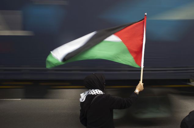 A woman holds a Palestinian flag as a truck passes by.
