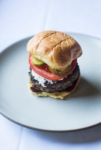 Hugh Acheson’s Cremini-Lamb Burger with Charred Scallions, Boursin, Pickles and Tomato on a Potato Roll. 