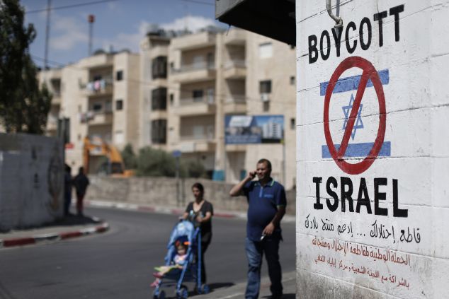 Palestinians walk past a sign painted on a wall in the West Bank biblical town of Bethlehem on June 5, 2015, calling to boycott Israeli products coming from Jewish settlements. The international BDS (boycott, divestment and sanctions) campaign, that pushes for a ban on Israeli products, aims to exert political and economic pressure over Israel's occupation of the Palestinian territories in a bid to repeat the success of the campaign which ended apartheid in South Africa. AFP PHOTO / THOMAS COEX