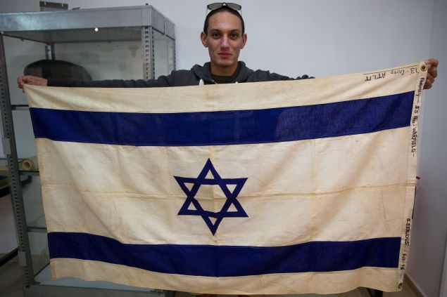 An employee of the Kedem Auction House in Jerusalem on November 15, 2015 shows the flag of the iconic ship the SS Exodus, the most famous of hundreds of ships that sought to transport European Jews to the land that later became the nation of Israel immediately after World War II. The flag will be sold at a public auction in December for at least 100,000 US dollars. AFP PHOTO/MENAHEM KAHANA