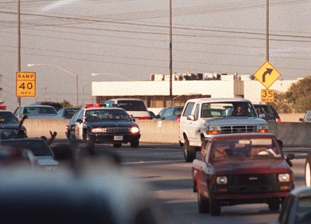 Motorists wave as police cars pursue the Ford Bronco (white, R) driven by Al Cowlings, carrying fugitive murder suspect O.J. Simpson, on a 90-minute slow-speed car chase June 17, 1994 on the 405 freeway in Los Angeles, California.