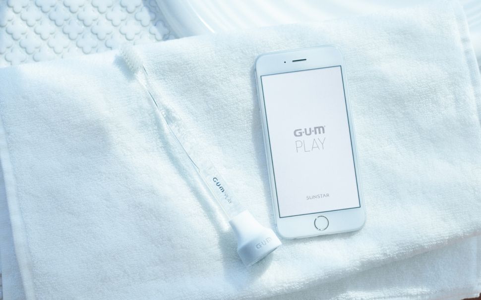 A toothbrush with a G-U-M Play attached, alongside the app. 