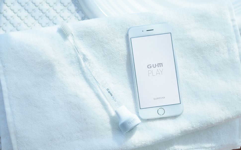 A toothbrush with a G-U-M Play attached, alongside the app.