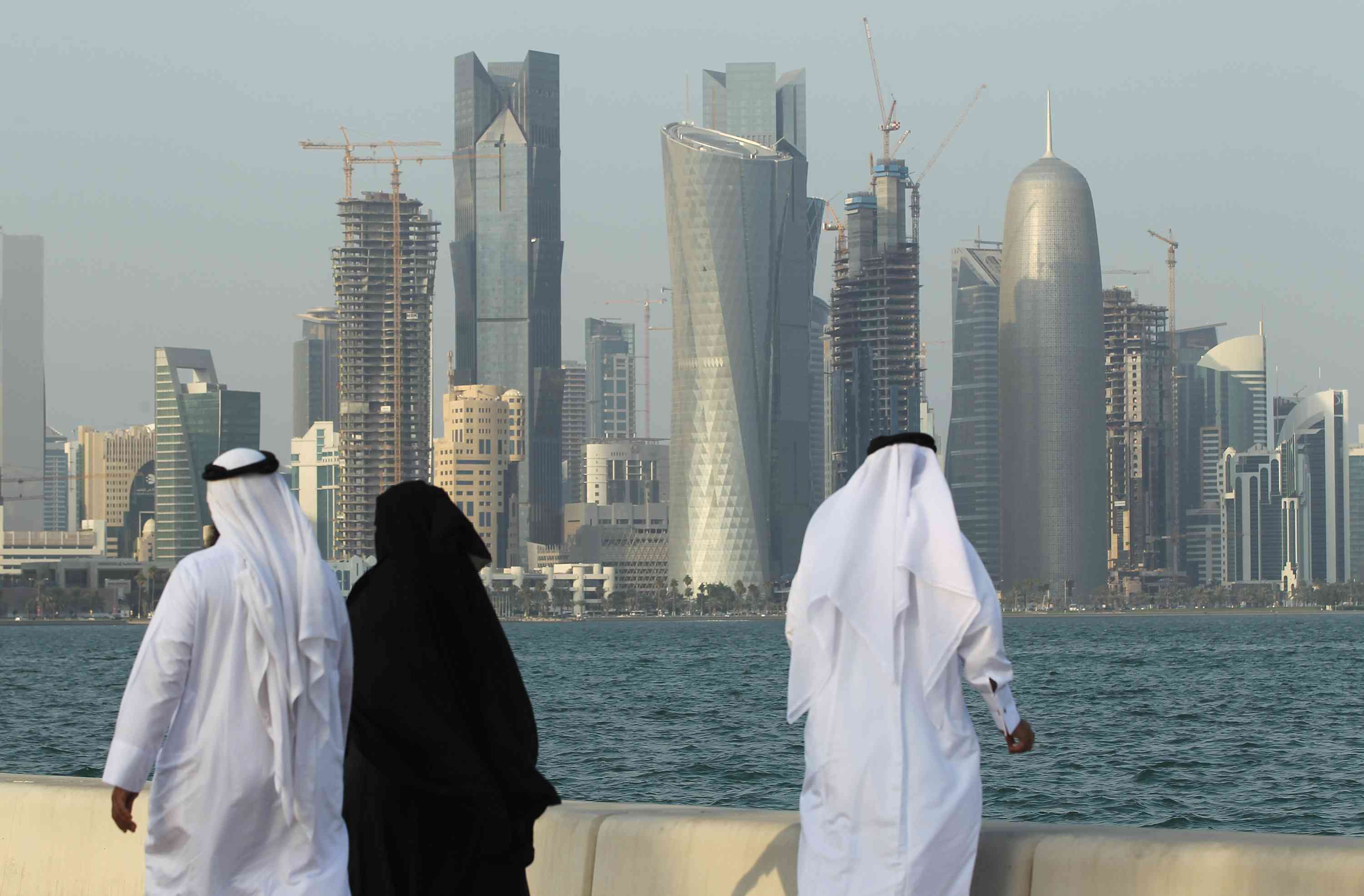 Men and women wearing traditional Qatari clothing visit the waterfront along the Persian Gulf across from new, budding financial district skyscrapers on October 24, 2011 in Doha, Qatar. Qatar will host the 2022 FIFA World Cup football competition and is slated to tackle a variety of infrastructure projects, including the construction of new stadiums.