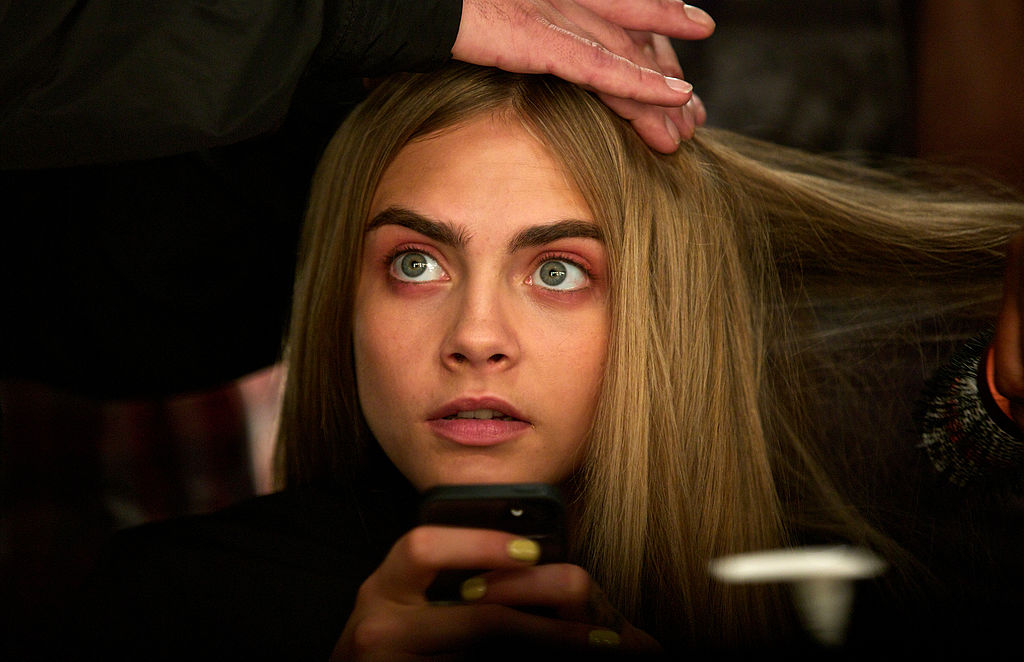 Cara Delevingne gets her hair done backstage ahead of the Burberry Prorsum 2014 Spring/Summer catwalk show during the London Fashion Week in London on September 16, 2013. AFP PHOTO / ANDREW COWIE