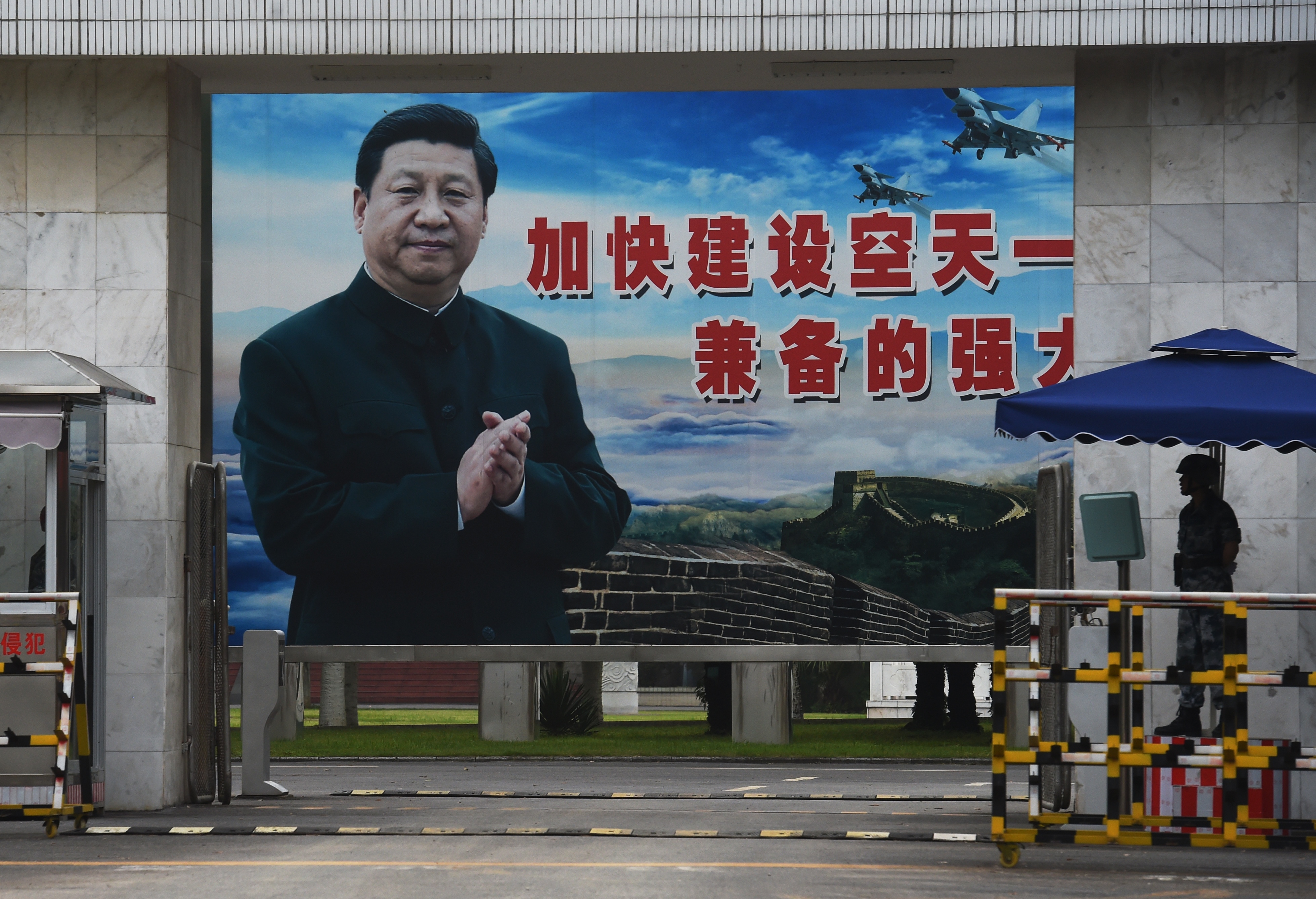 A soldier stands guard in front of a huge portrait of Chinese President Xi Jinping at the entrance to a military base in Guilin, in China's southern Guangxi region on May 13, 2016. The slogan reads "Speed up the establishment of a powerful people's Air Force and sharpen offensive and defensive capabilities". / AFP / GREG BAKER