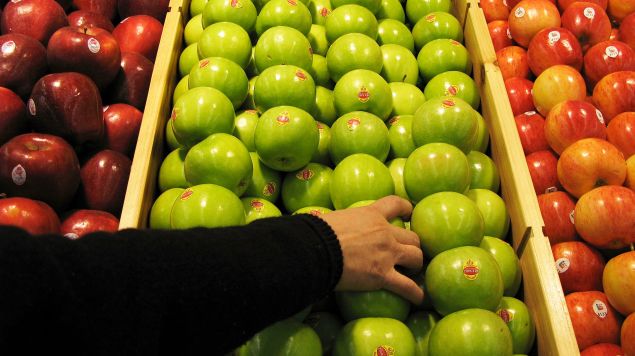 A shopper chooses granny smith apples.