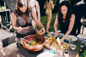 Two attendees make use of the cutting board and tongs.