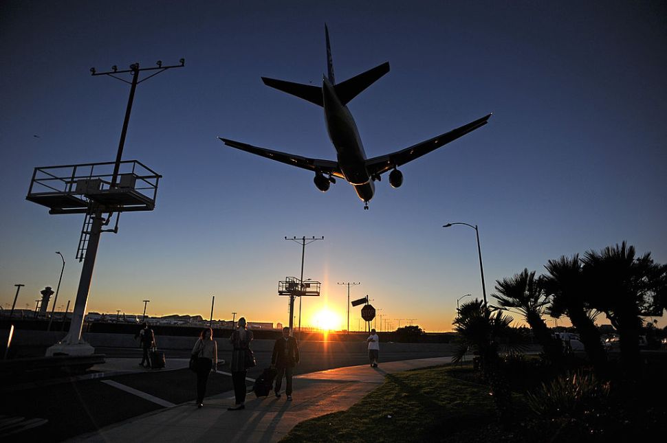 Passengers pull their luggage outside Los Angeles International Airport (LAX) as a plane comes in for a landing at dusk November 1, 2013 in Los Angeles, California. Earlier in the day a gunman opened fire with an assault rifle inside the airport, killing a security agent, creating scenes of chaos and causing widespread flight disruptions. AFP PHOTO / ROBYN BECK