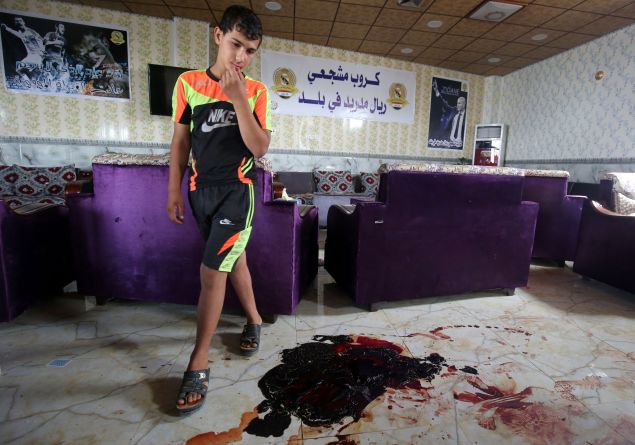 TOPSHOT - An Iraqi boy walks past the blood stains and debris at a cafe, that was popular with local fans of Spain's Real Madrid football club, in the Balad area, north of the capital Baghdad, on May 14, 2016, a day after a deadly raid claimed by Islamic State group militants. At least 16 people were killed and 30 wounded, including several members of the security forces, in the attack in the town of Balad and the ensuing chase, officials said. / AFP / AHMAD AL-RUBAYE