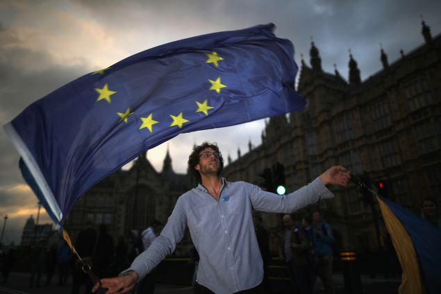 LONDON, ENGLAND - JUNE 28: A protester waves an EU flag in front of the Houses of Parliament as they demonstrate against the EU referendum result on June 28, 2016 in London, England. Up to 50,000 people were expected before the event was cancelled due to safety concerns. Early evening up to 2000 people have still converged on the square and then marched to Parliament to vent their anti-Brexit feelings. 