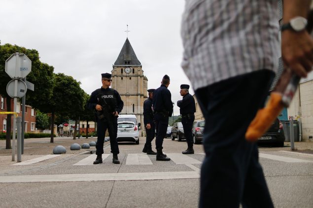 A man carries a French baguette as police officers stand guard the Saint-Etienne church on July 27, 2016 in Saint-Etienne-du-Rouvray, 125 kilometres (77 miles) north of Paris, where a priest was killed the day before in the latest of a string of attacks against Western targets claimed by or blamed on the Islamic State jihadist group. Father Jacques Hamel, a semi-retired assistant parish priest, had his throat slit in a church in northern France on July 26, 2016, after two men stormed the building and took hostages. As the two attackers made to leave the church they were confronted by a French police unit specialising in hostage situations, the BRI, and were shot dead. 