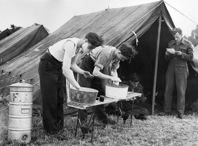 8th July 1944: RAF ground staff wash and shave at tin basins after a day's work refitting Spitfire aircraft at their squadron's camp.