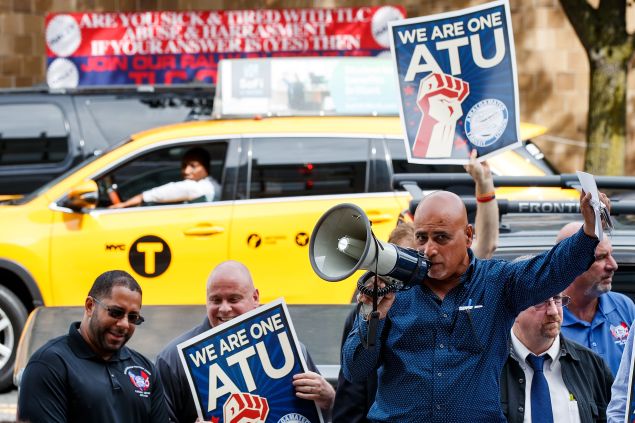 A New York City taxi cab drives by as Syed Manzar, who drives for both Uber and Lyft, speaks during a rally to call on the New York City Taxi and Limousine Commission to force Uber and Lyft to hold union elections, September 27, 2016 in the Queens borough of New York City.