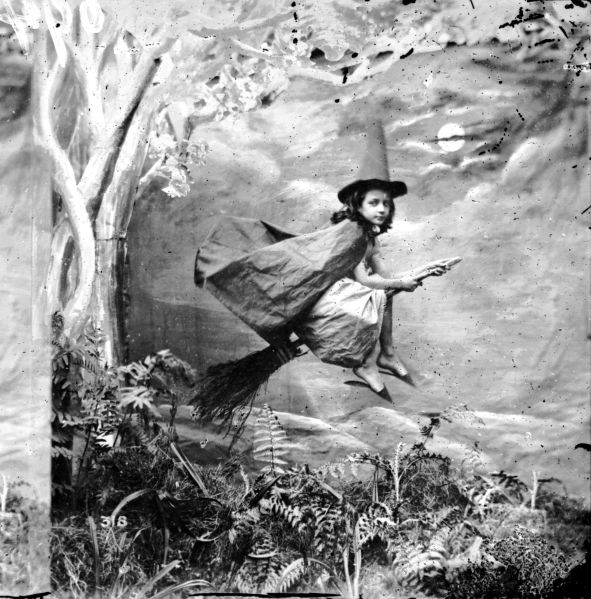 A young girl dressed as a witch suspended mid-air on a broomstick circa 1865.