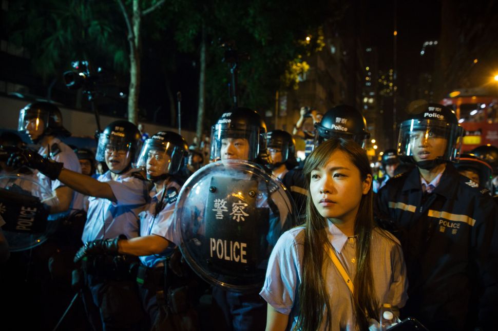Yau Wai-ching of the stands in front of riot police amid ongoing protests in Hong Kong. China has blocked Yau from taking her elected seat in Hong Kong's legislature for her separatist beliefs.