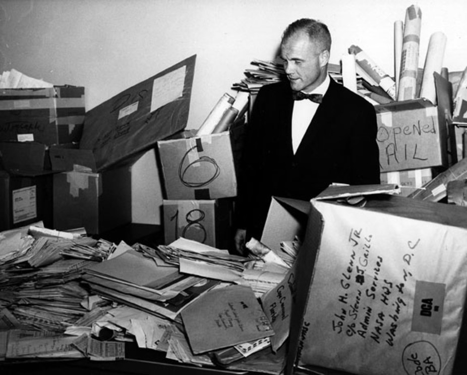John Glenn stands in the NASA mail room surrounded by thousands of letters sent to him.